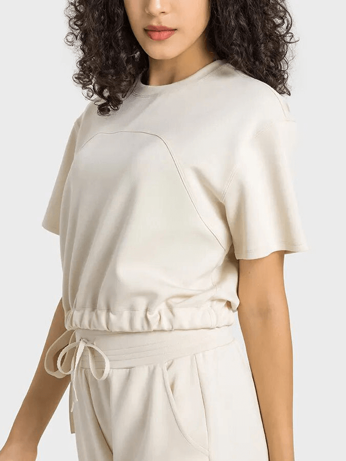 Woman wearing a beige sports short sleeve crop T-shirt with adjustable hem, ideal for fitness activities like yoga and running.